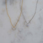 Gold and silver minimalist tiny bezel pendant necklaces on a marble background.
