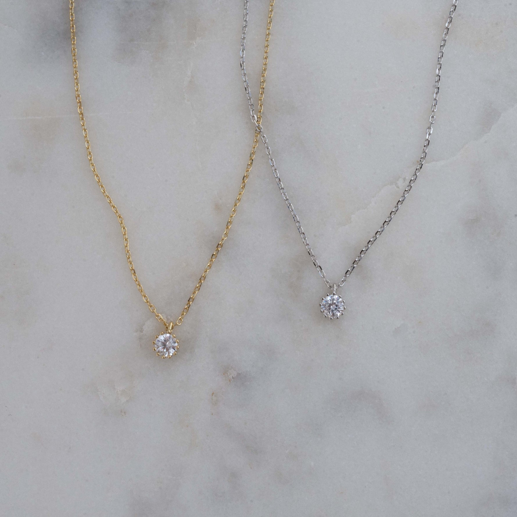 Gold and silver minimalist tiny bezel pendant necklaces on a marble background.