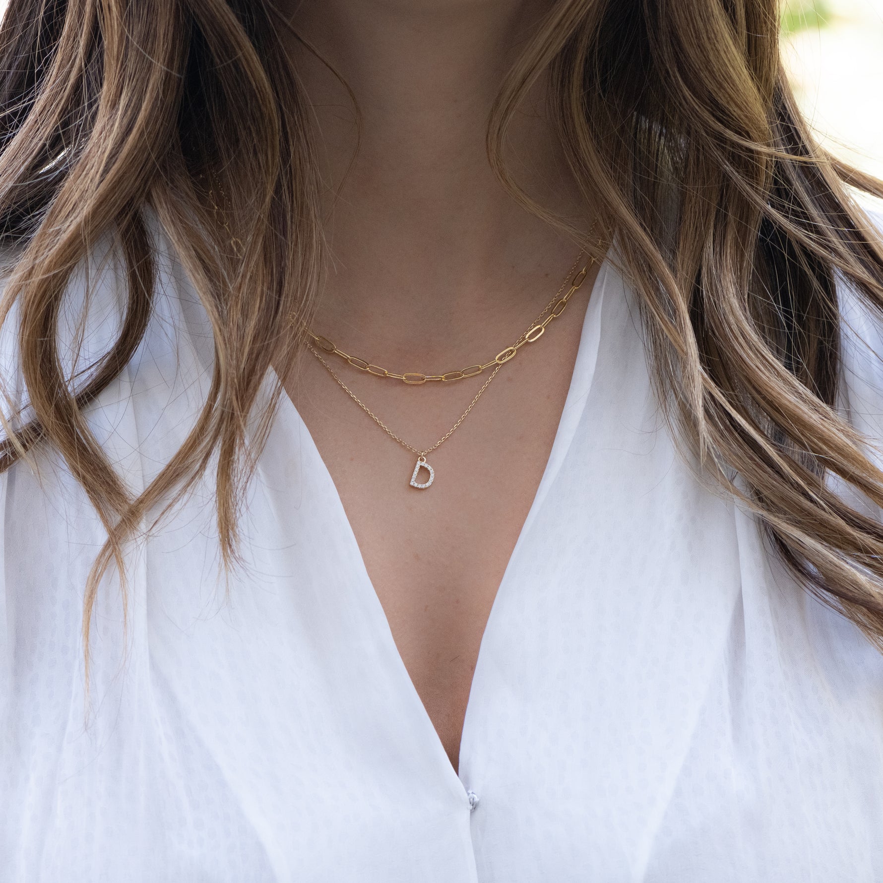 Model wearing a paperclip chain necklace layered with an initial letter gold pendant necklace.