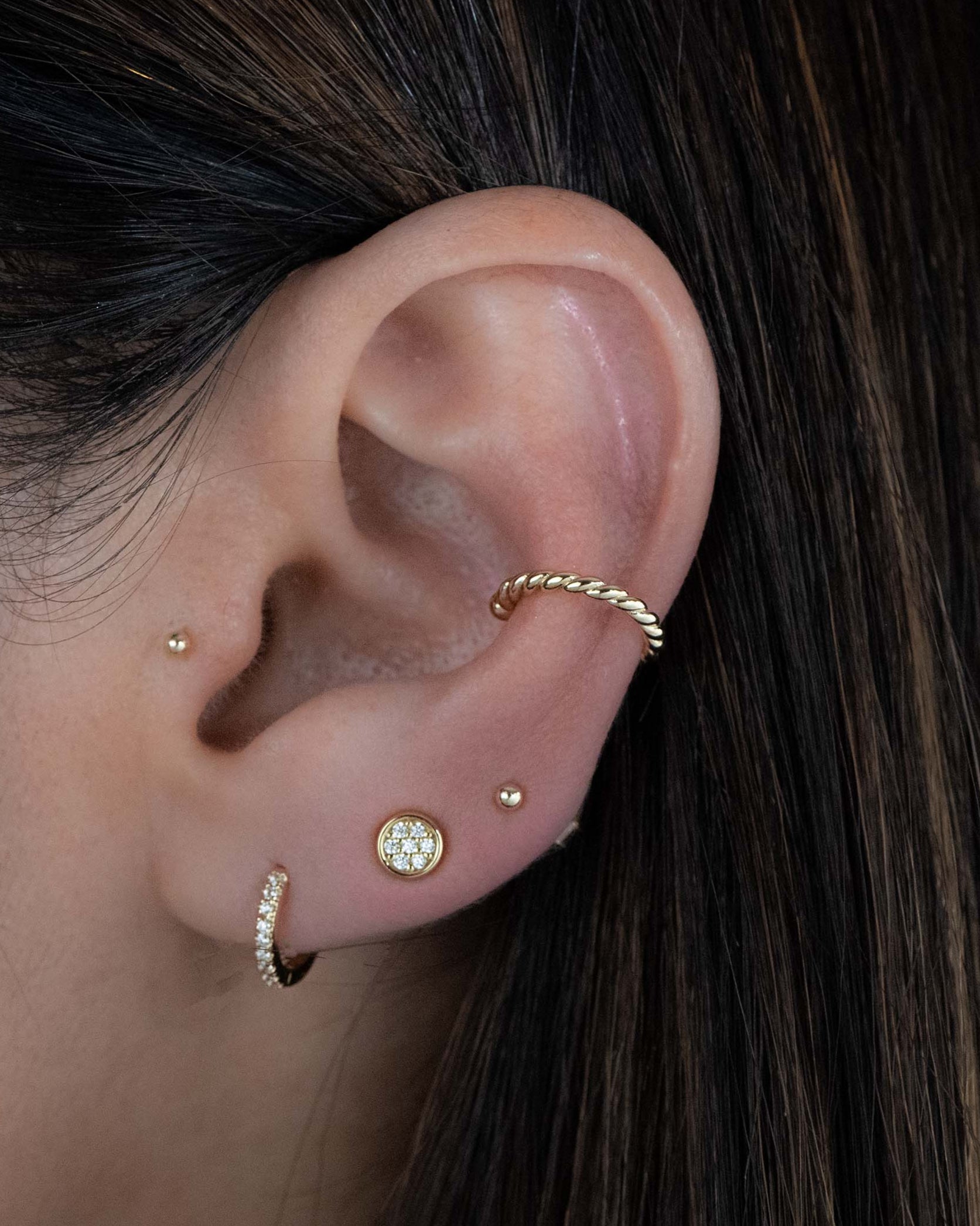 Model wearing gold studs with a pave huggie and a spiral ear cuff.