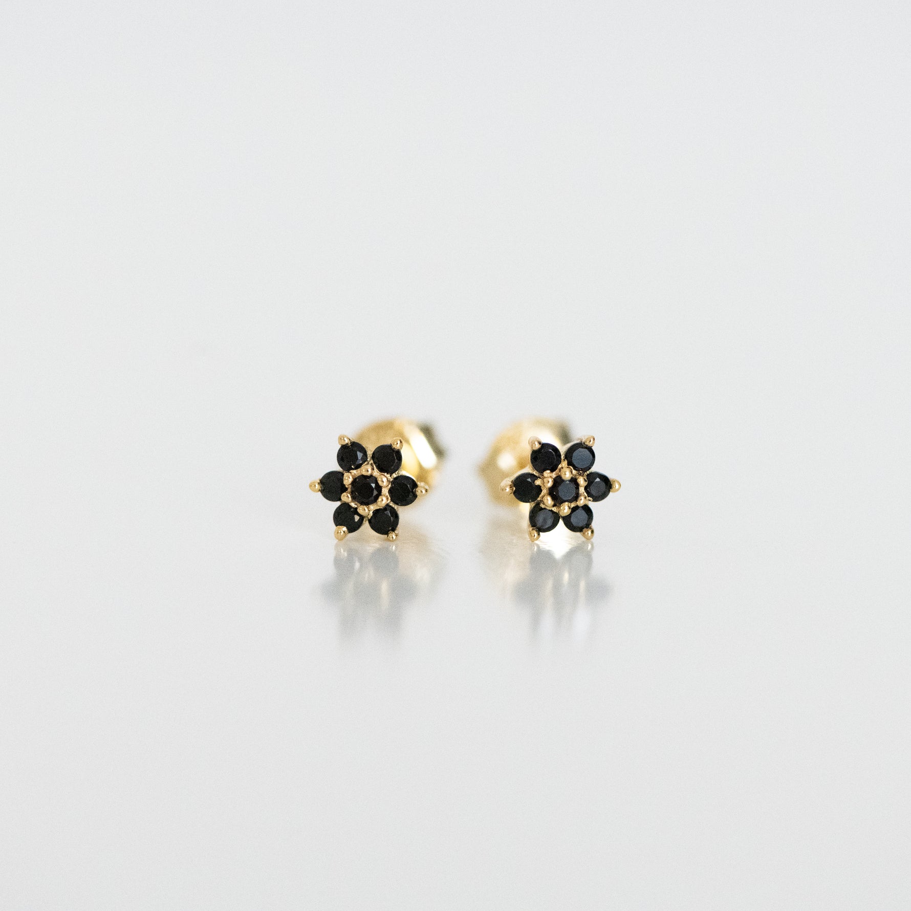 Upclose shot of gold dainty flower stud earrings in black. 