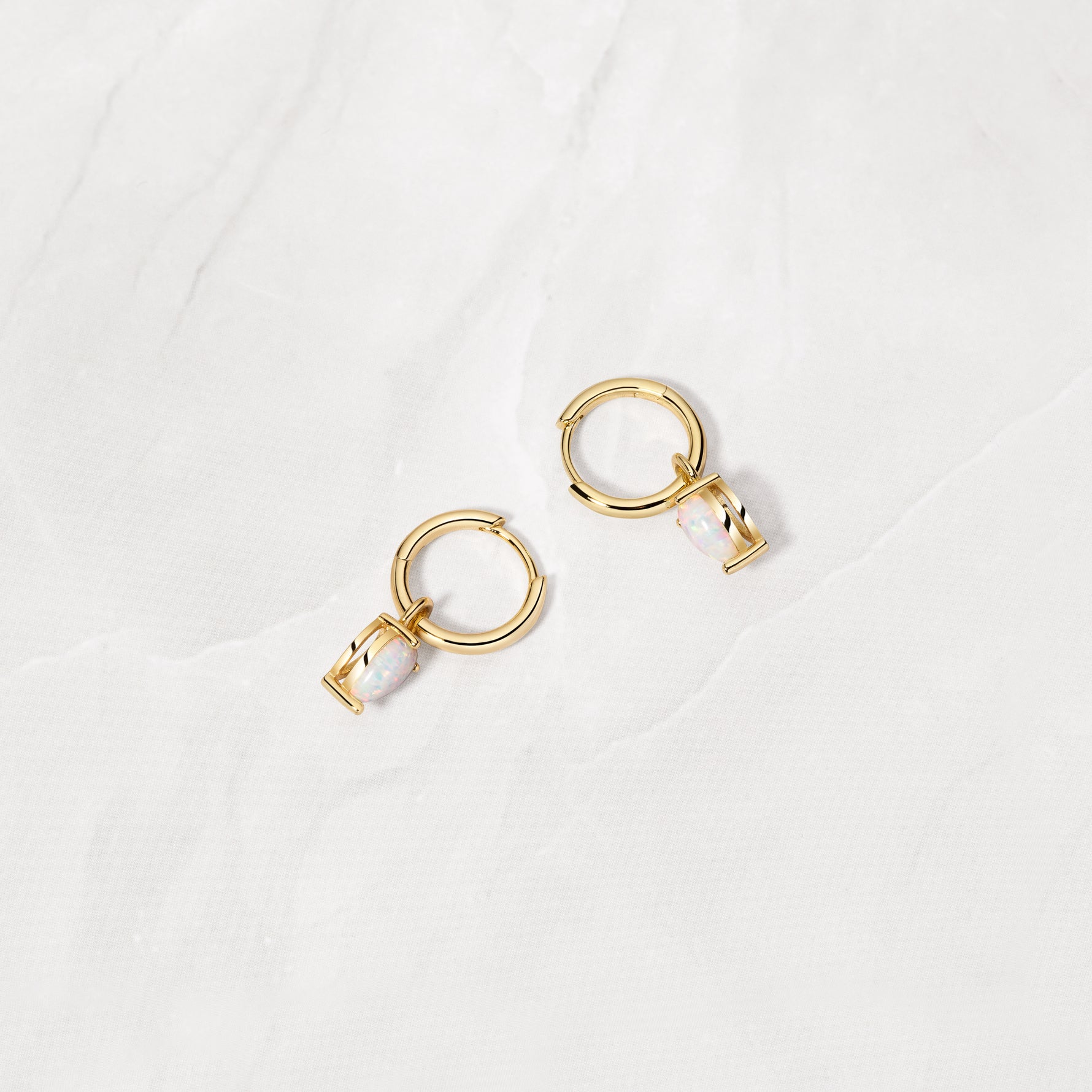 Gold opal charm huggie earrings from the side angle. 