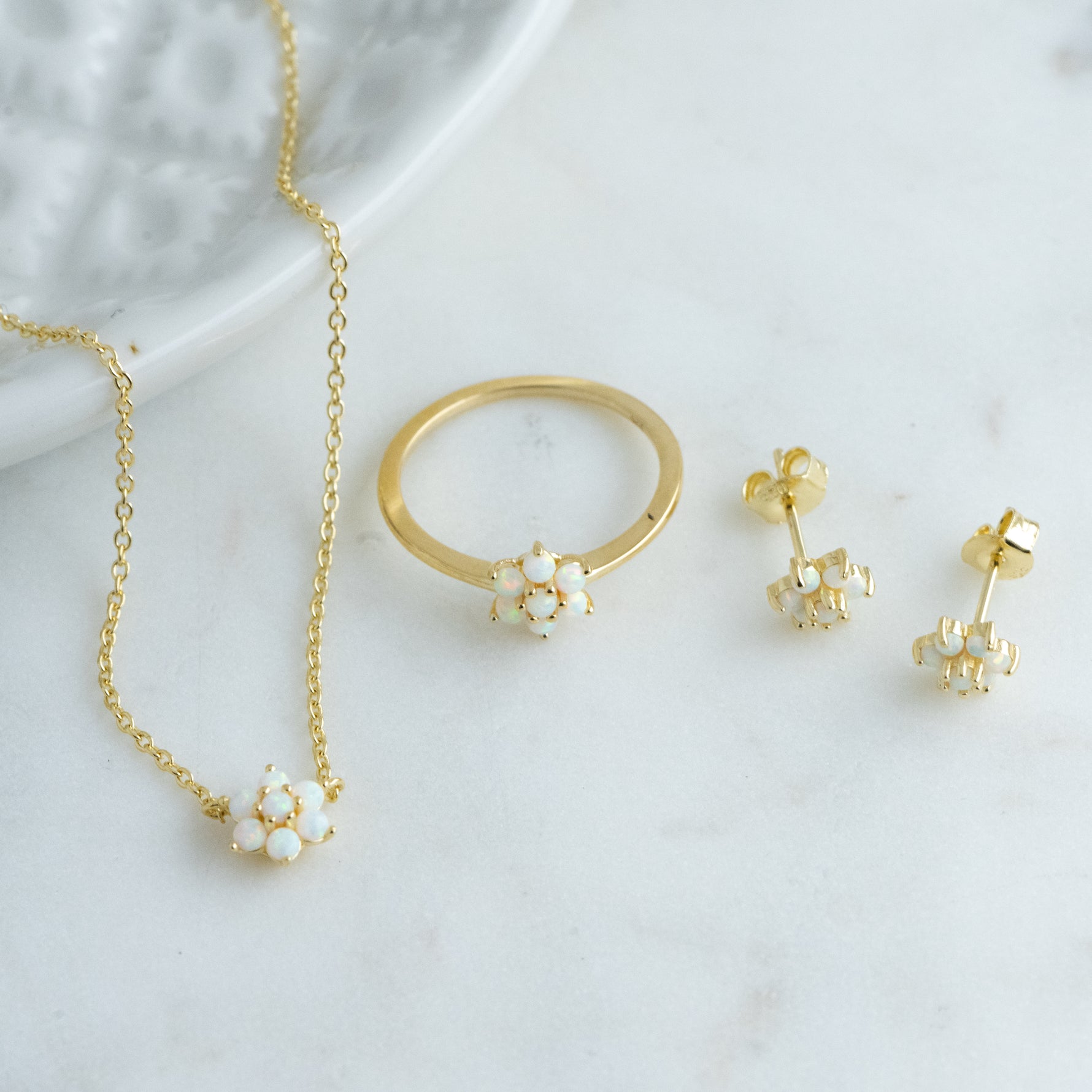 Opal flower gold jewelry set featuring a chain necklace, a opal flower ring, and opal flower stud earrings on a marble background.
