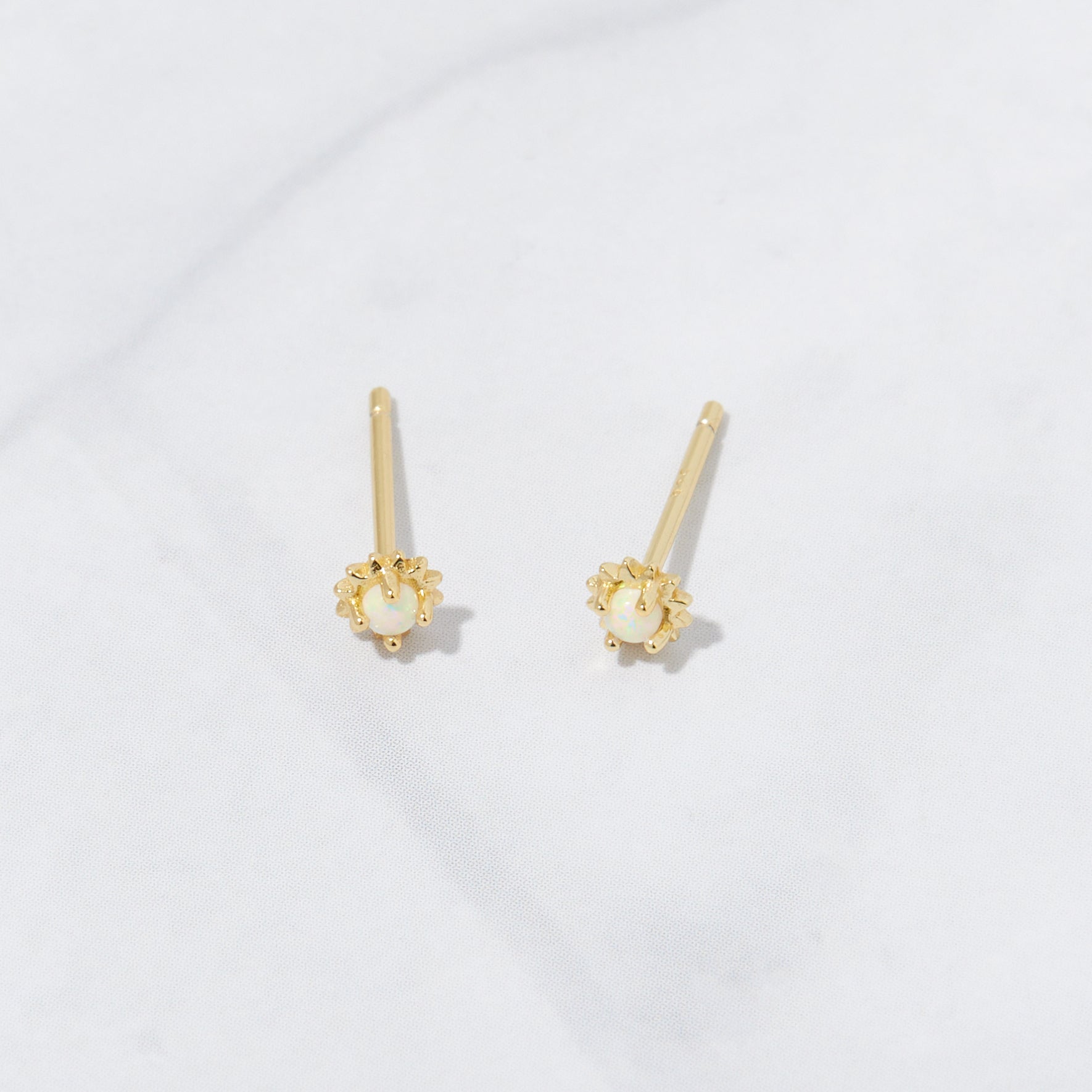 Tiny 14k gold plated opal vibrant stud earrings on marble background.