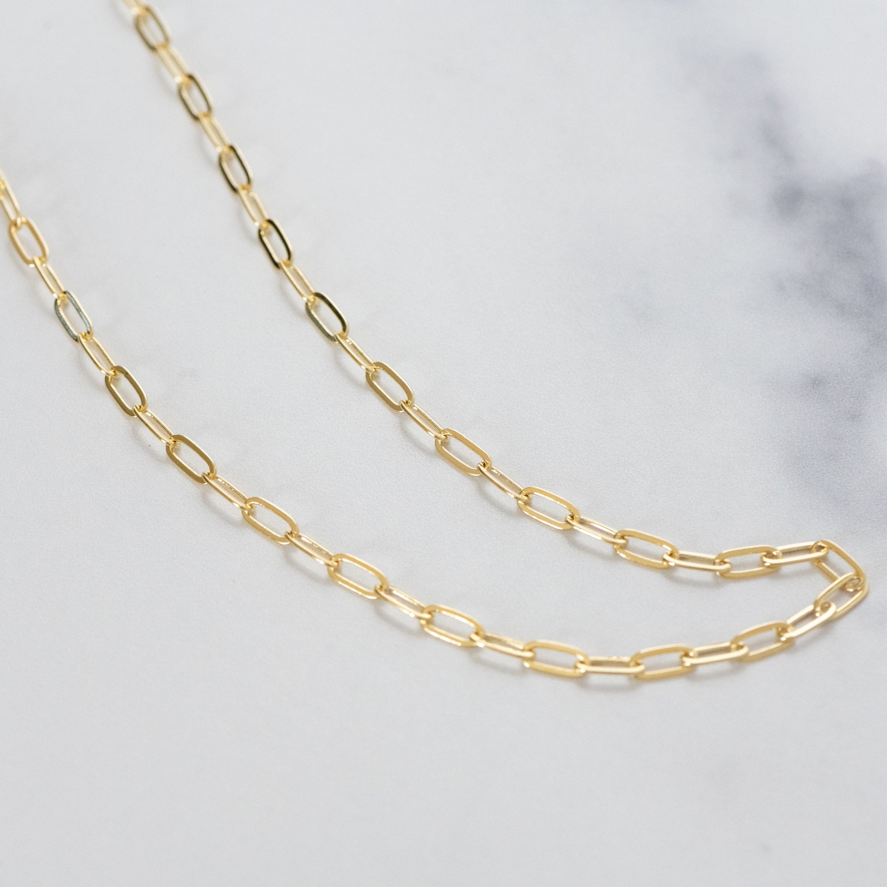 Gold paperclip chain necklace on a marble background
