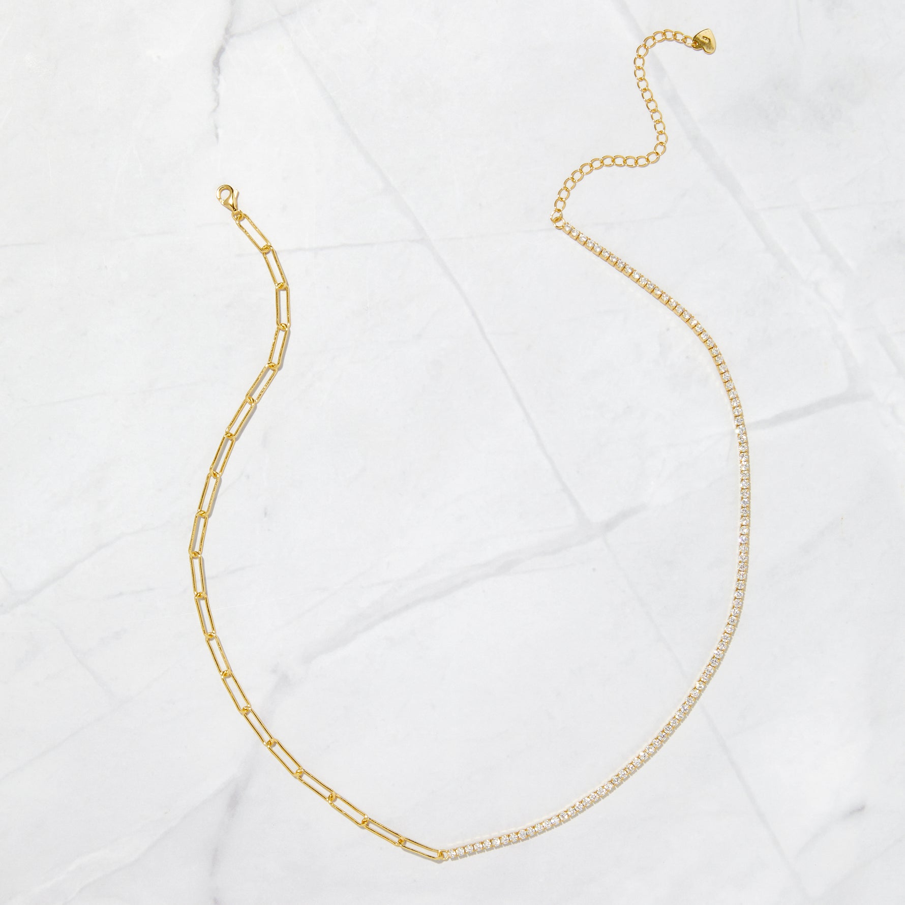 Gold paperclip tennis chain necklace on a marble backdrop. 