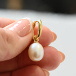 Model holding gold pearl dangle hoop earrings