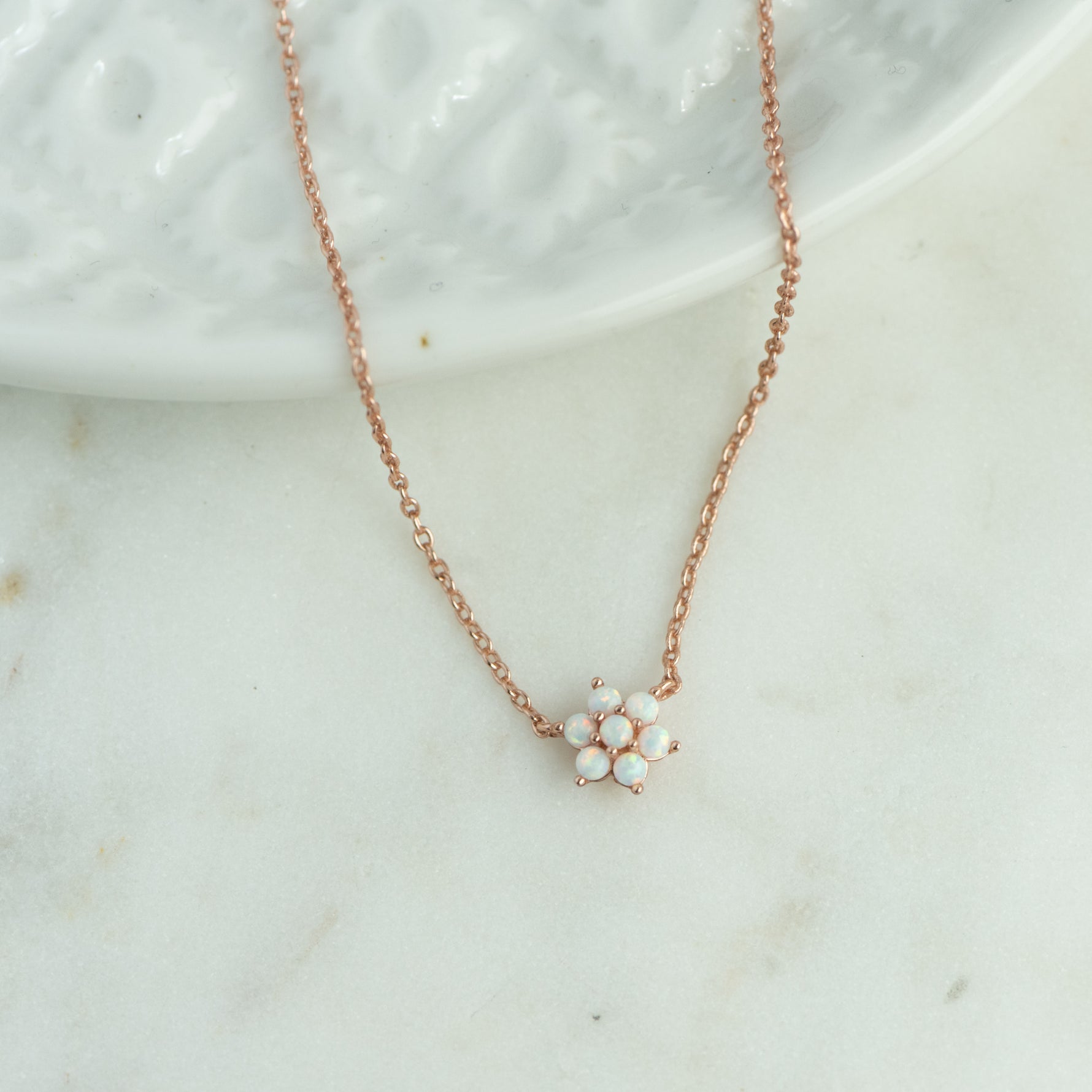 Rose gold opal flower pendant necklace on marble background.