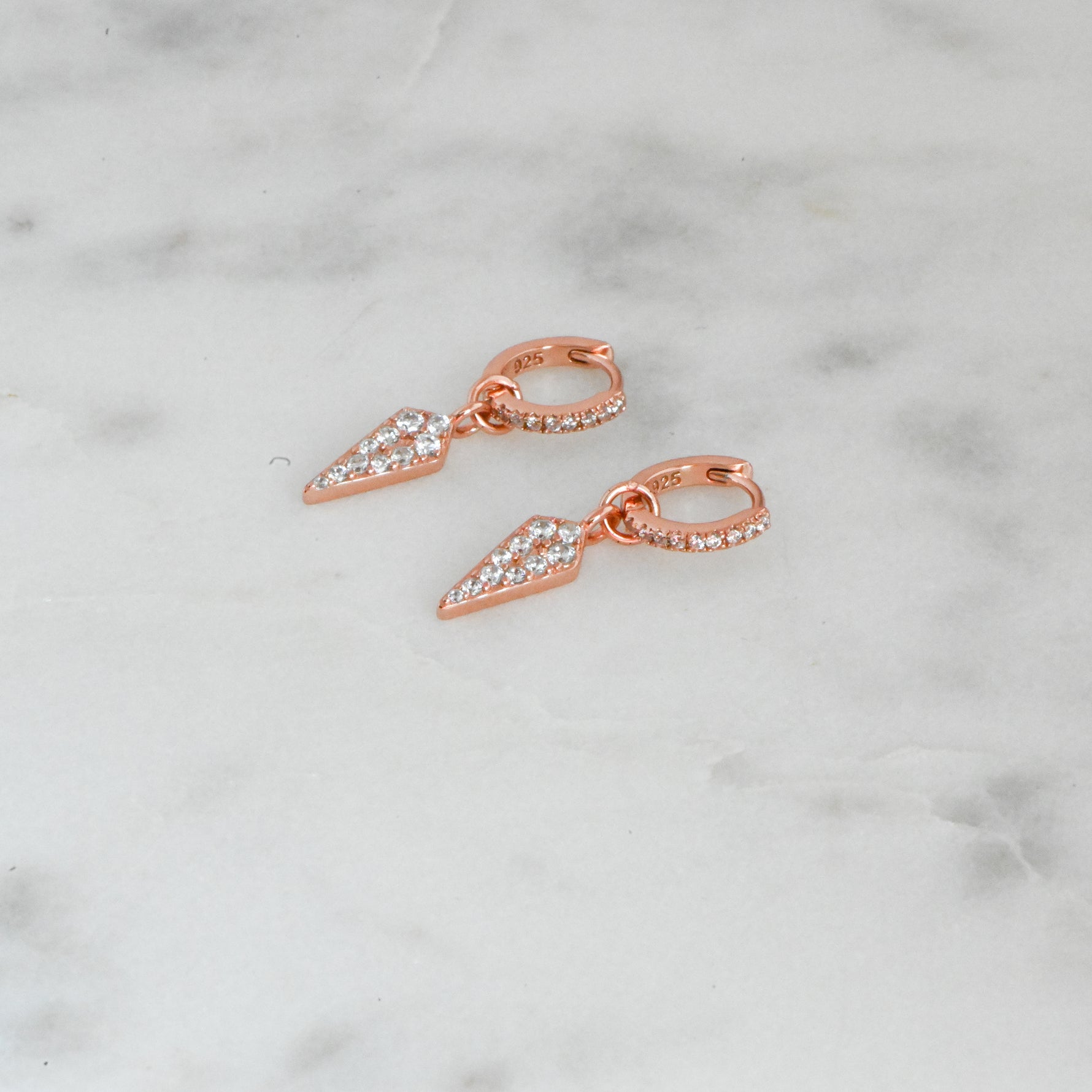 Rose gold delicate spike charm huggie hoop earrings on marble background.