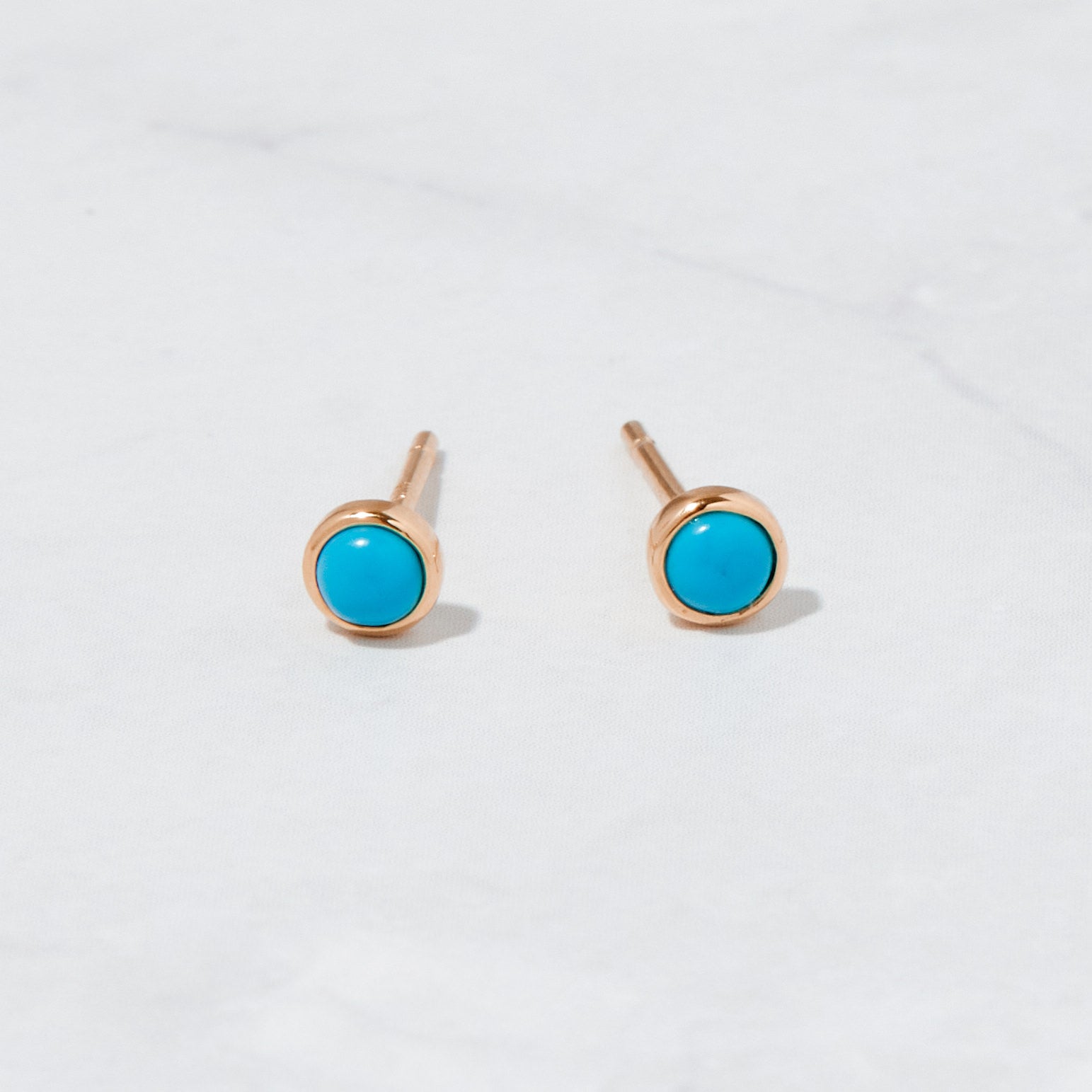 Rose gold turquoise stud earrings on marble background.