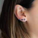 Model wearing sapphire flower studs paired with a sapphire baguette stud.