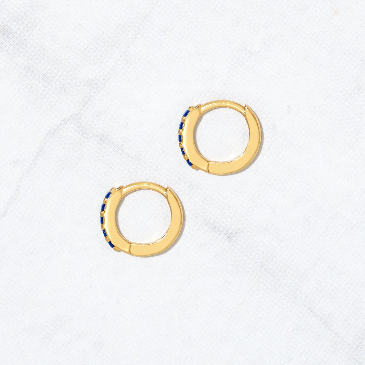 Sapphire birthstone earrings from the side on marble background.