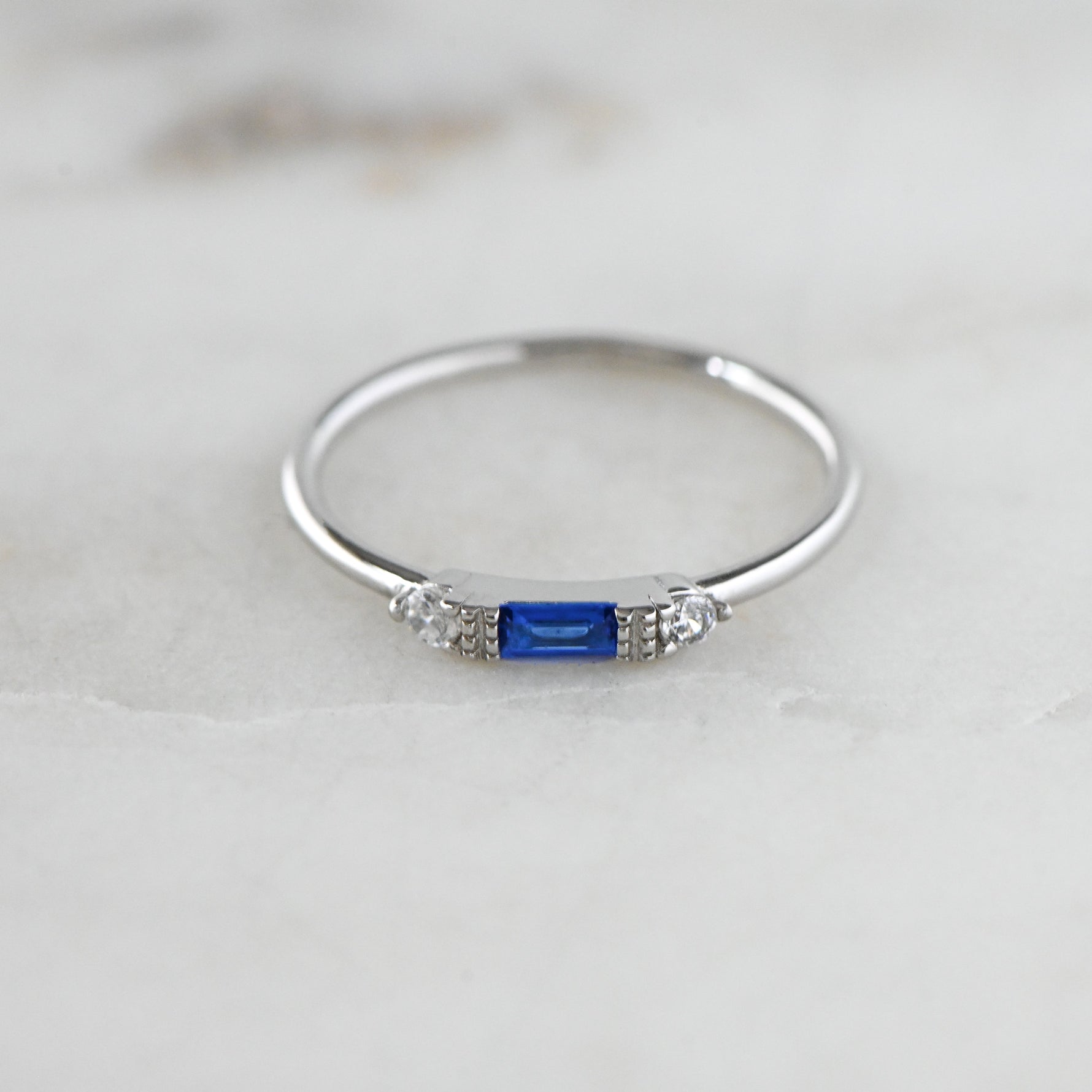 Sterling silver dainty sapphire baguette thin ring in soft studio lighting. 