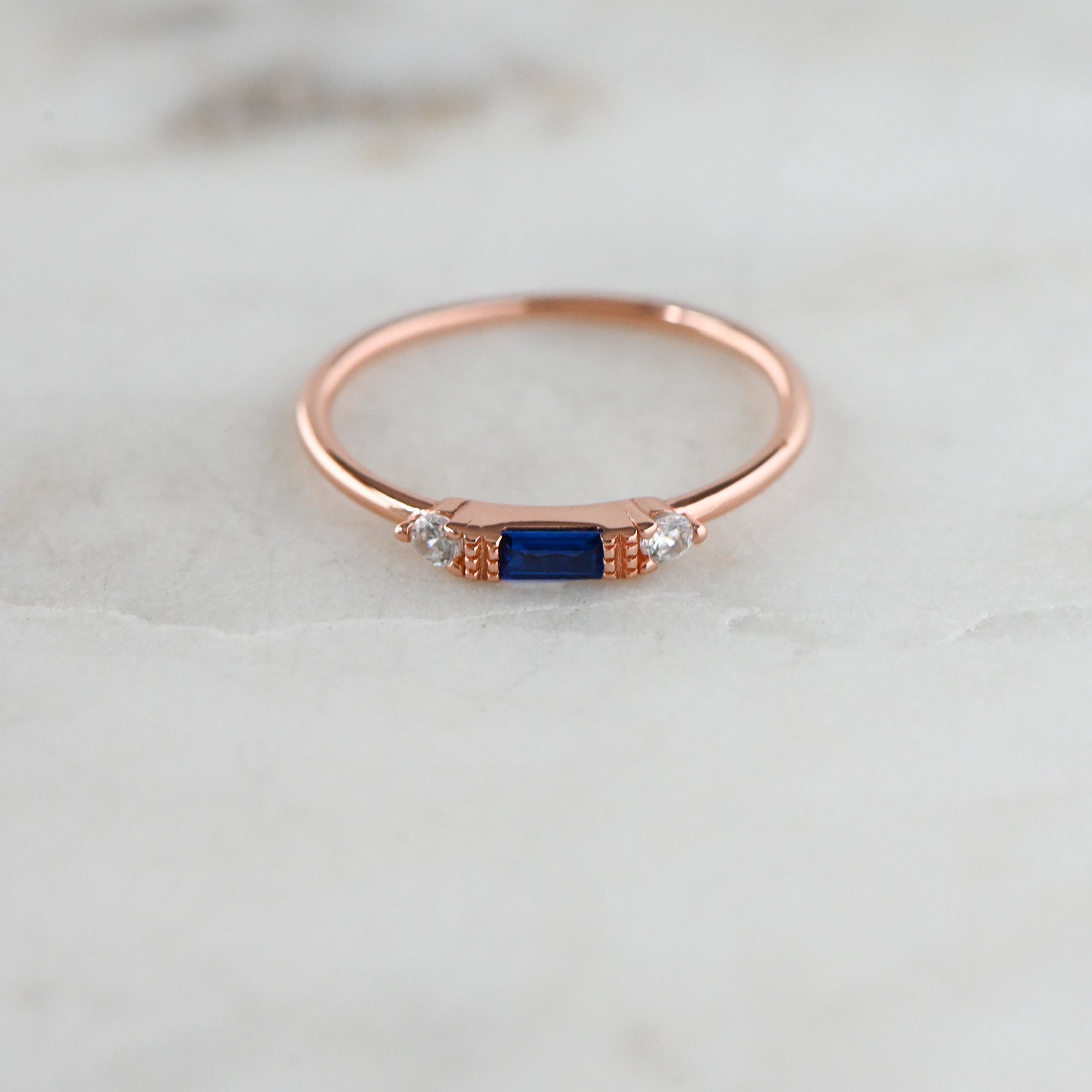 Dainty rosegold birthstone sapphire ring on marble background. 