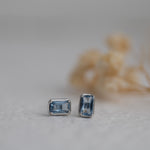 Closeup image of dainty silver aquamarine baguette stud earrings. 
