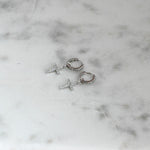 Delicate silver diamond cross huggies on marble background