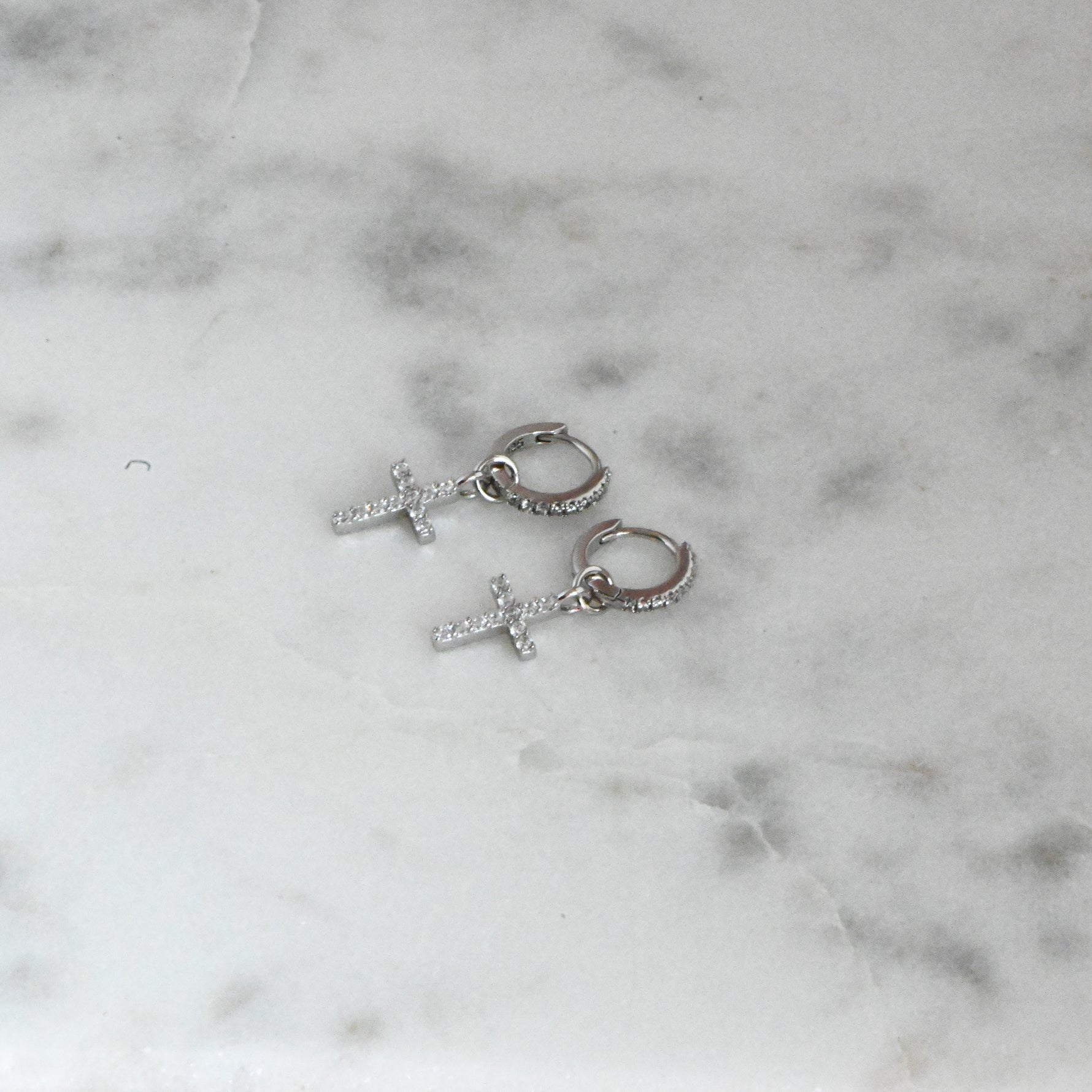 Delicate silver diamond cross huggies on marble background