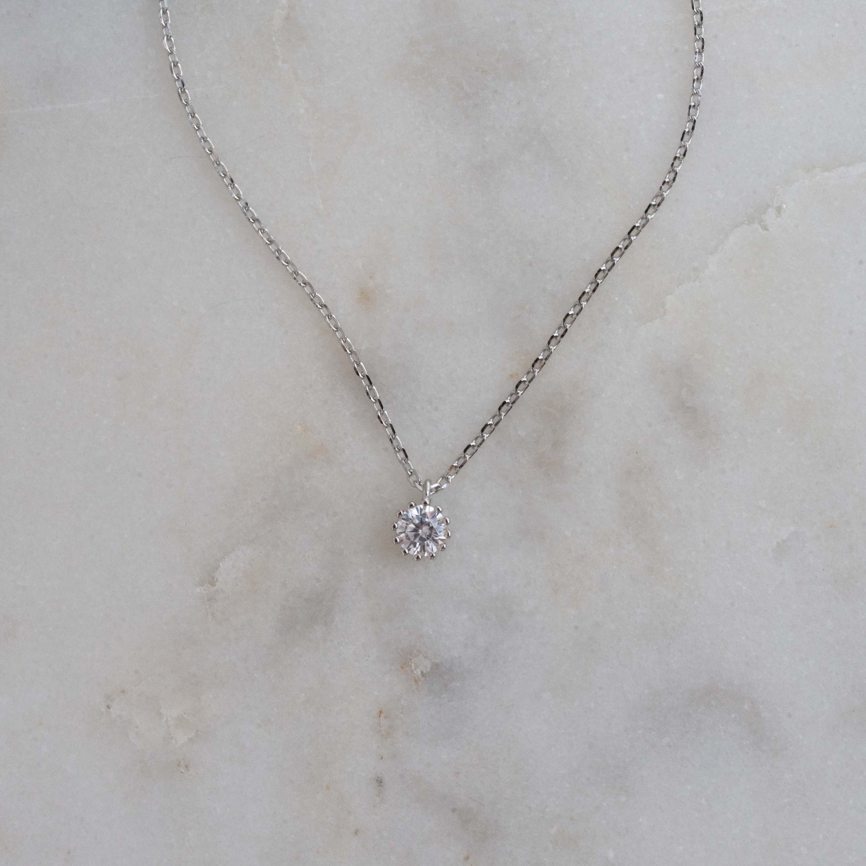 Dainty silver round bezel pendant necklace on marble background