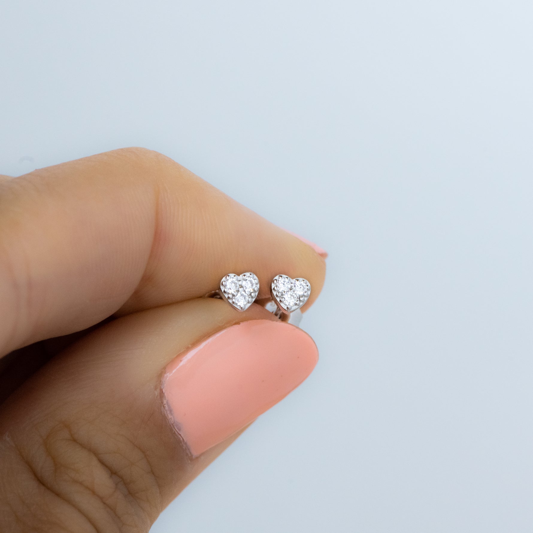 Model holding dainty sterling silver cz heart earrings. 