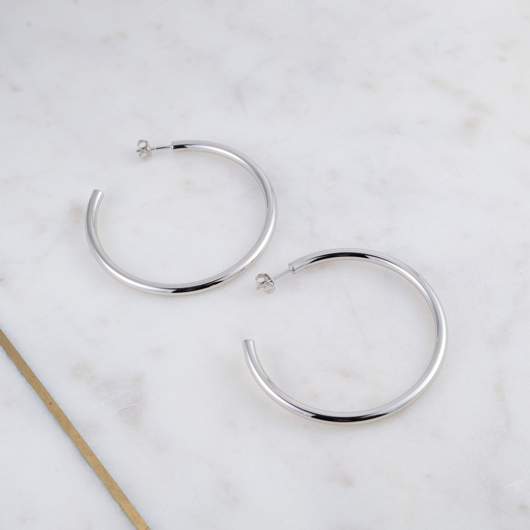 Large sterling silver lightweight hoop earrings on marble background.