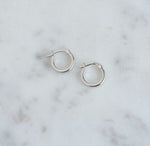Small silver flat hoop earrings on marble background.