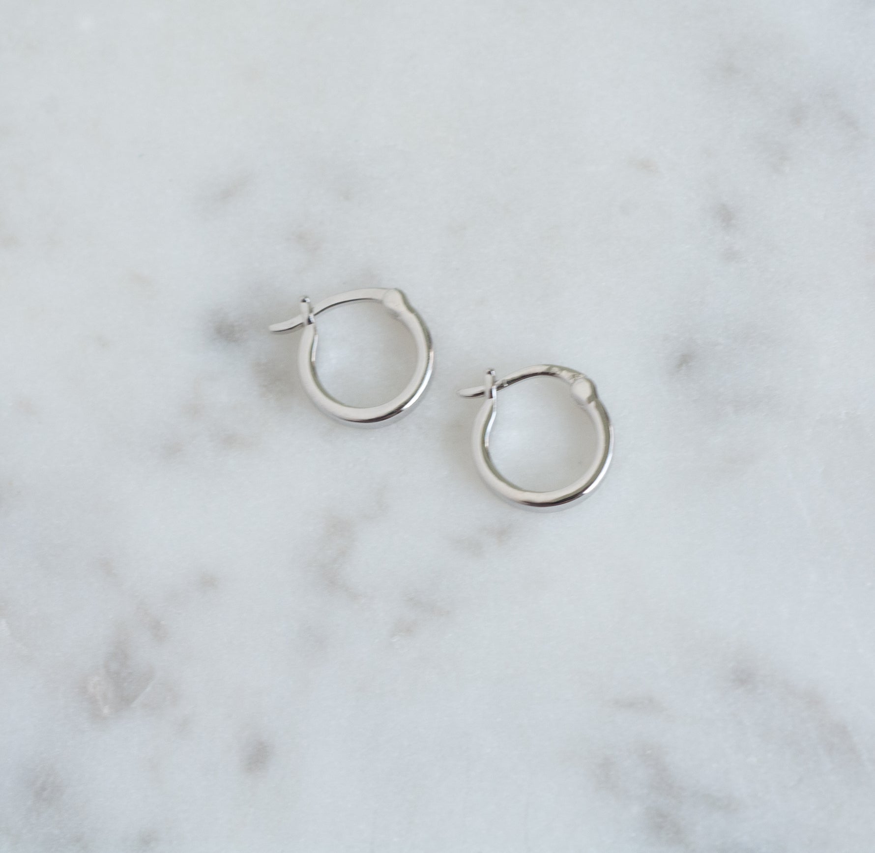 Small silver flat hoop earrings on marble background.