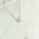 Close-up of dainty silver opal flower pendant necklace on marble background