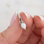 Dainty sterling silver opal charm huggie hoops in model's hand.