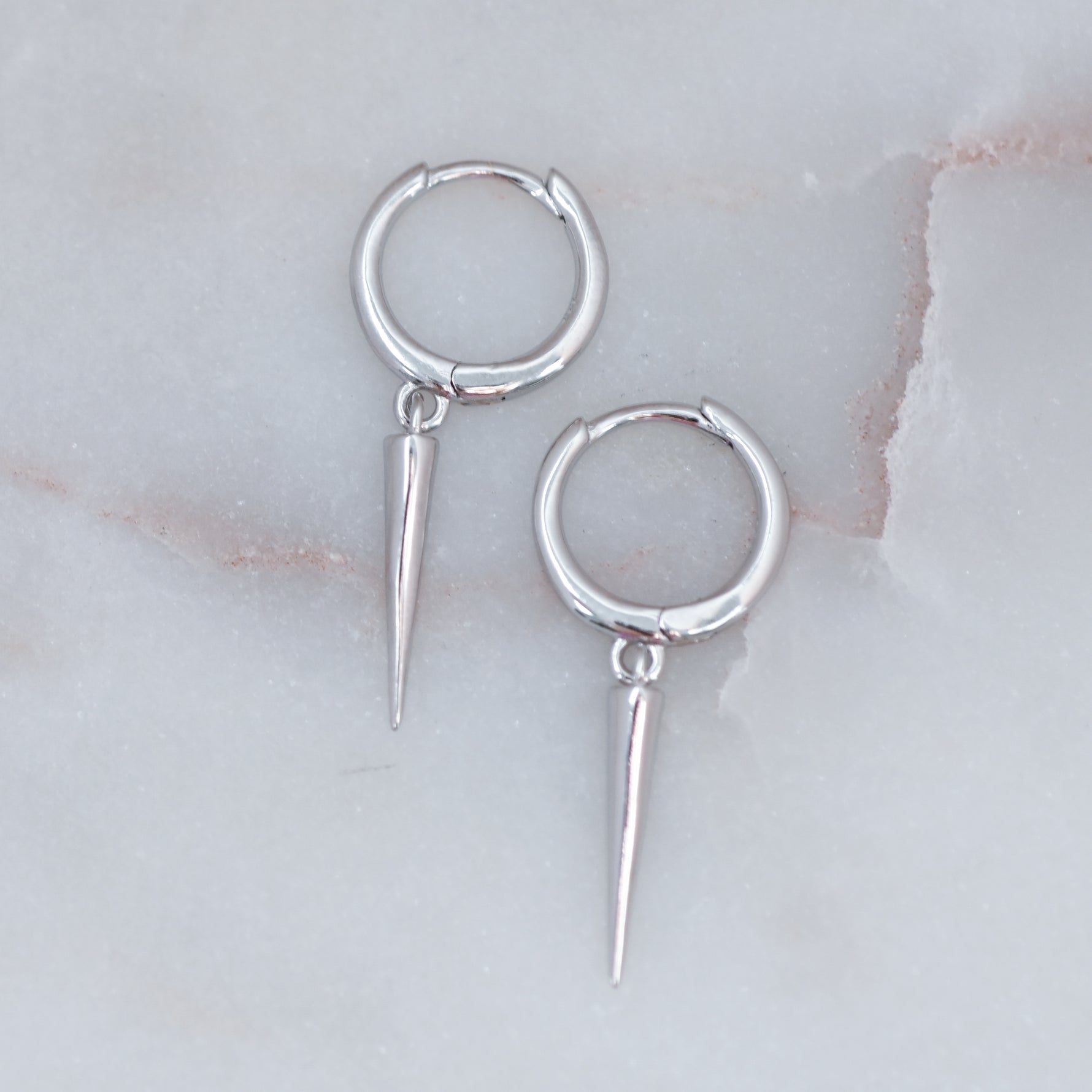 Delicate sterling silver spike charm huggie earrings on marble background
