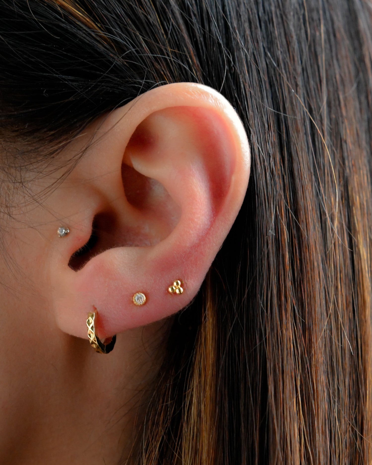 Model wearing tiny geometric hammered huggie earrings in a minimalist earring stack.