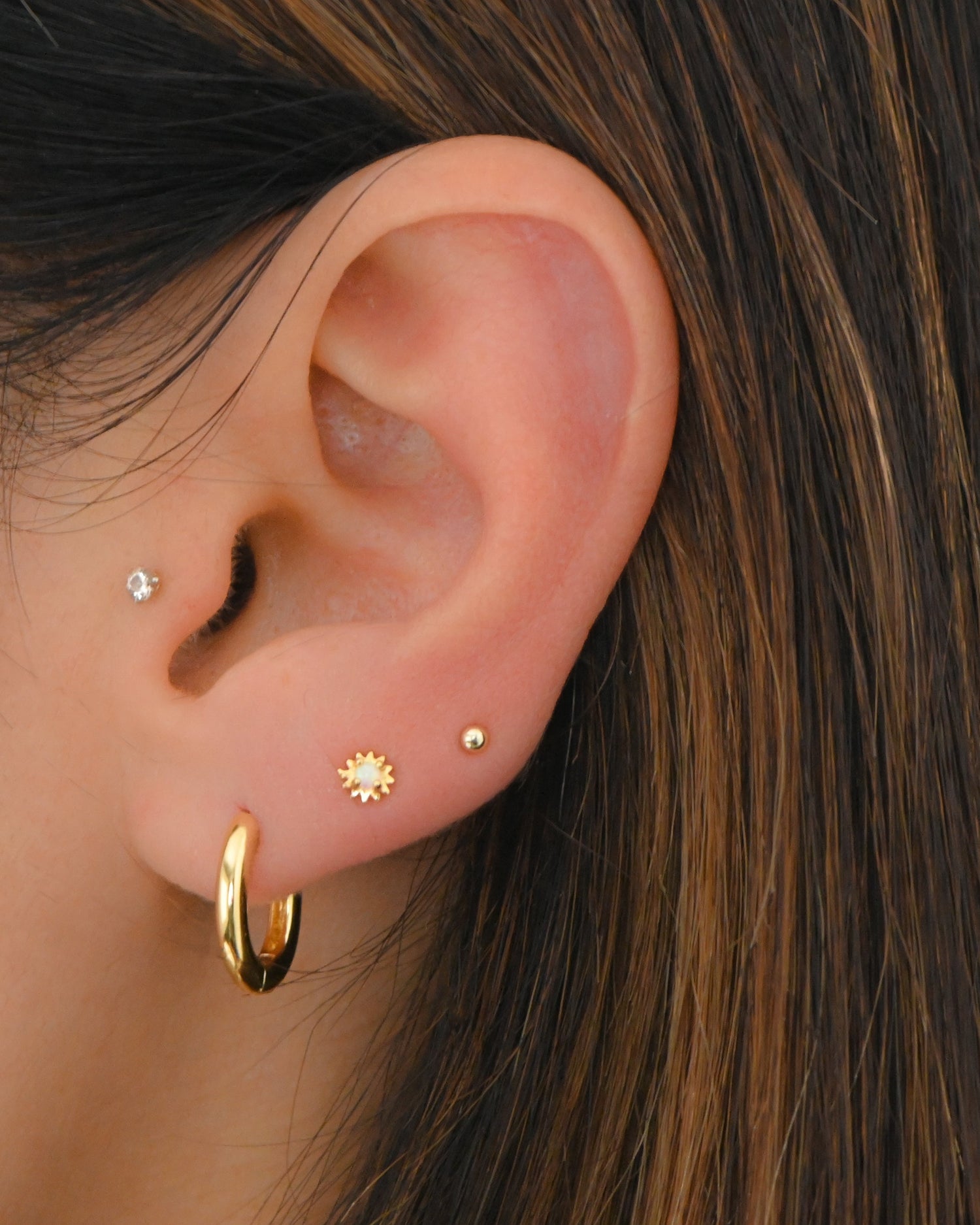 Model wearing gold sleek oval hoops, tiny opal starburst studs, and ball studs