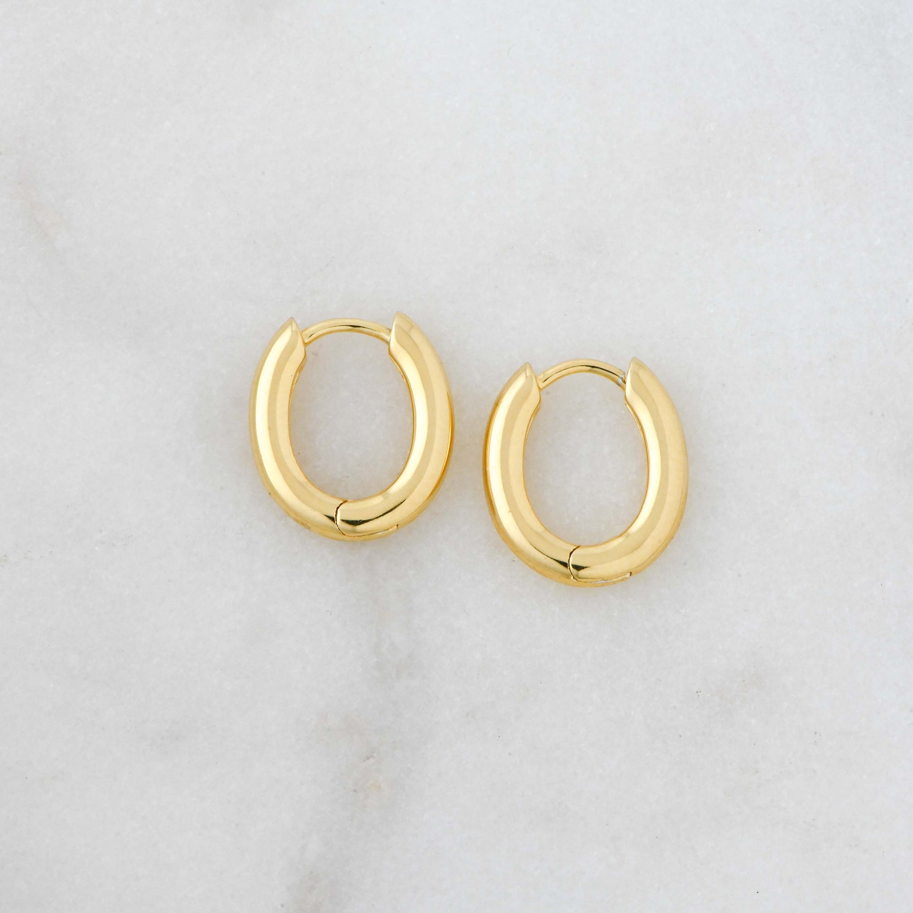 Small gold huggie hoops with an oval shape