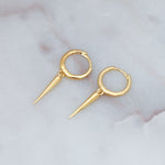 Delicate gold spike charm huggie earrings on marble background