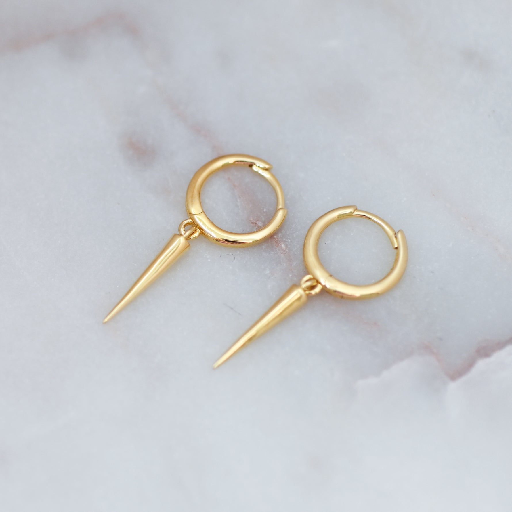 Delicate gold spike charm huggie earrings on marble background