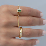 Model wearing gold ring stack including an emerald ring, a thin spiral band, and a bezeled dome ring. 