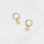 Gold star charm earrings on marble background.