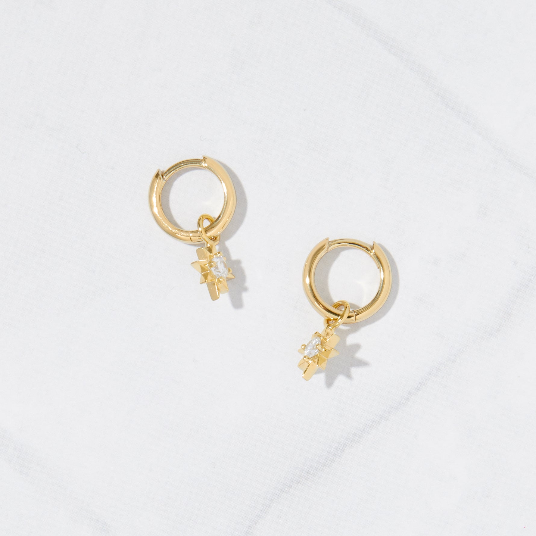 Gold star charm earrings on marble background.
