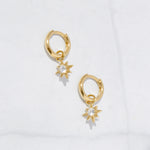 Tiny gold sunburst charm huggie earrings with cz charms dangling.