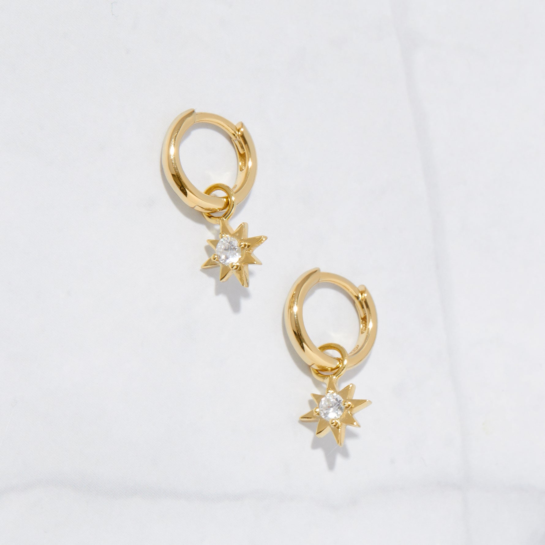 Tiny gold sunburst charm huggie earrings with cz charms dangling.