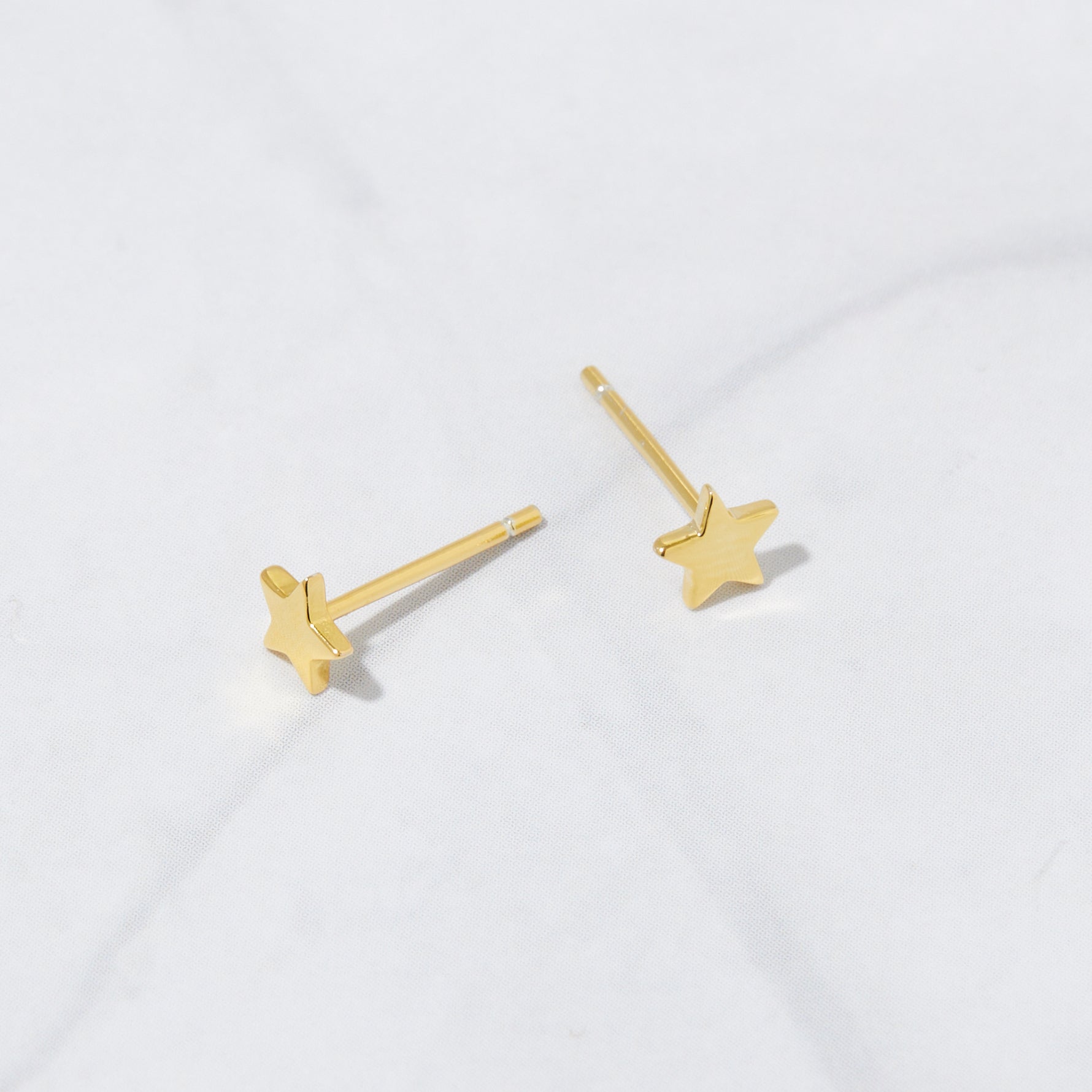 Up-close image of gold plain star stud earrings from the above angle, revealing the gold post. 