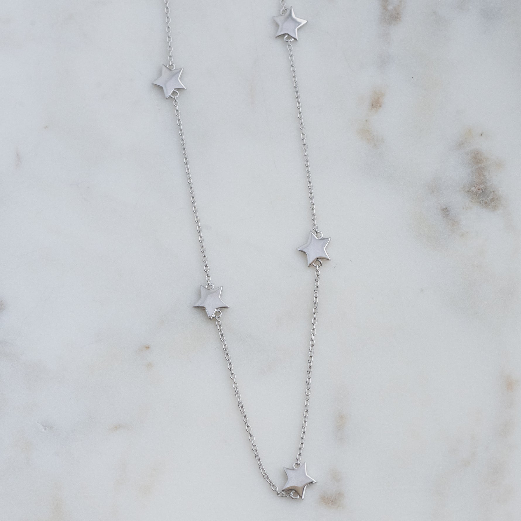 Dainty sterling silver plain star collar necklace on marble background.