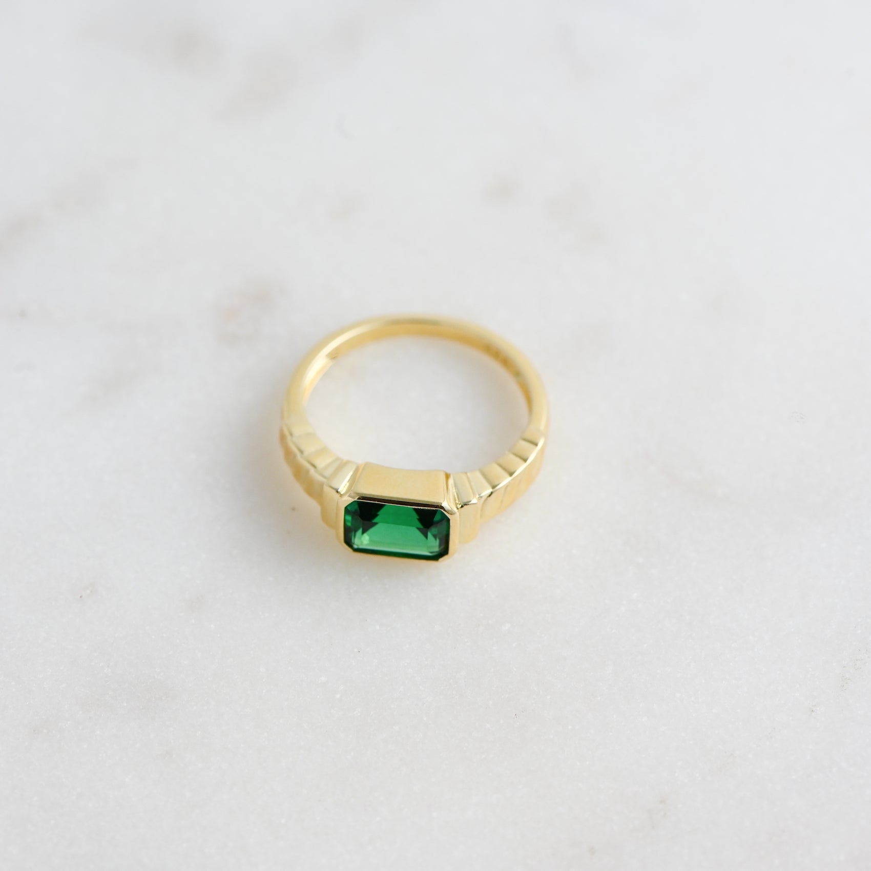 Statement emerald ring from the side in soft studio lighting on a marble background. 