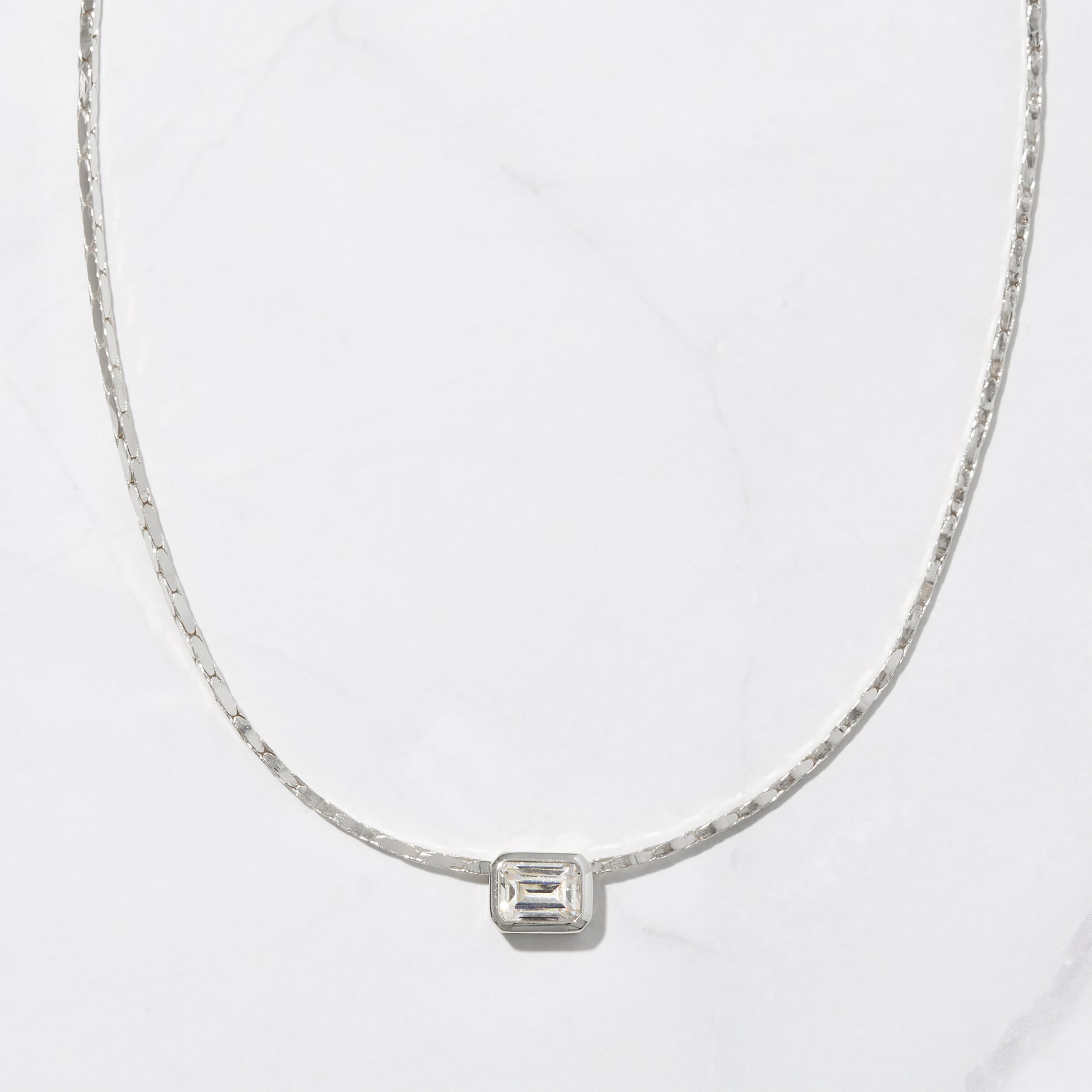 Silver baguette bezel pendant necklace on marble background