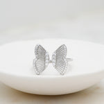 Delicate statement silver butterfly ring on a white plate. 