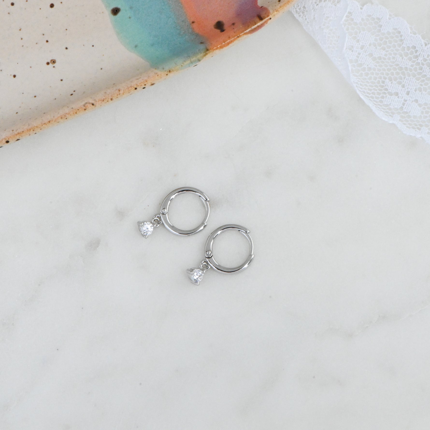 Delicate silver cz bezel huggie hoop earrings on marble background.