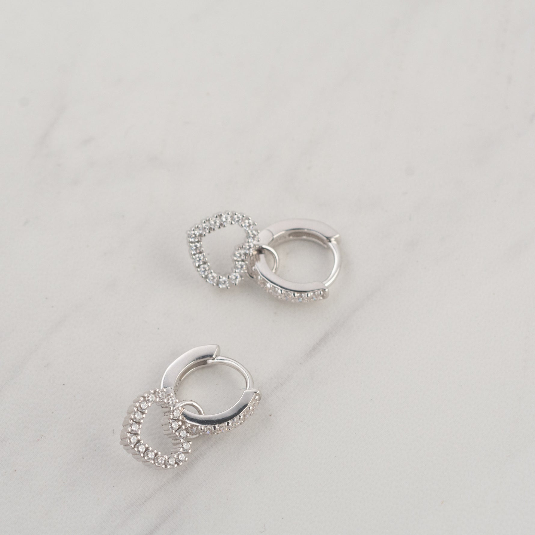 Silver dainty heart charm huggie hoop earrings upclose.