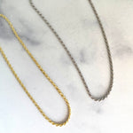 Thin gold and silver rope chain necklaces on marble surface.