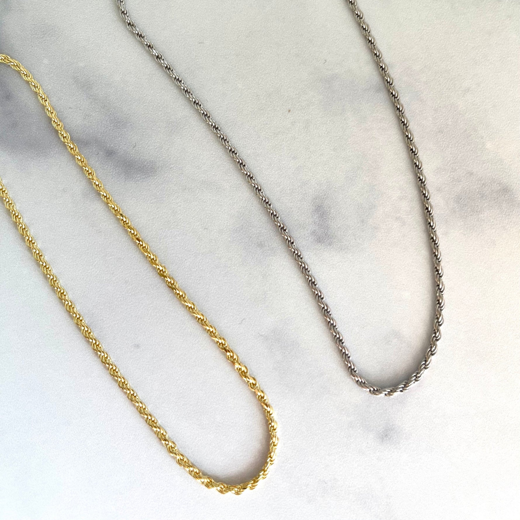 Thin gold and silver rope chain necklaces on marble surface.