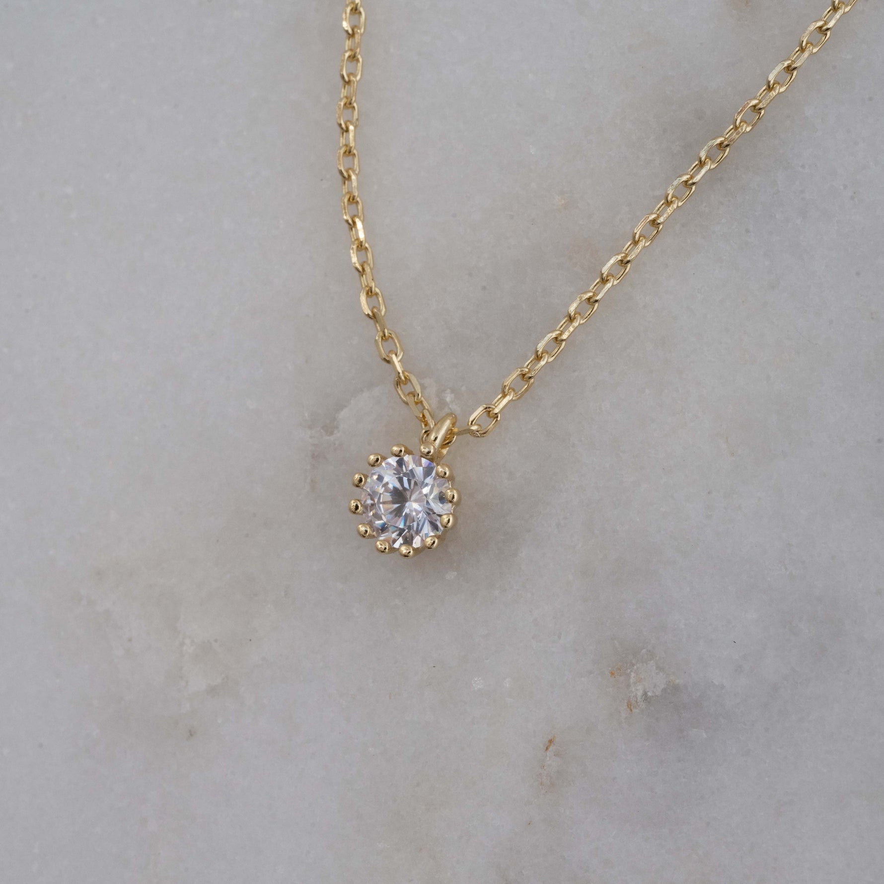 Tint round diamond pendant necklace in gold on a marble background