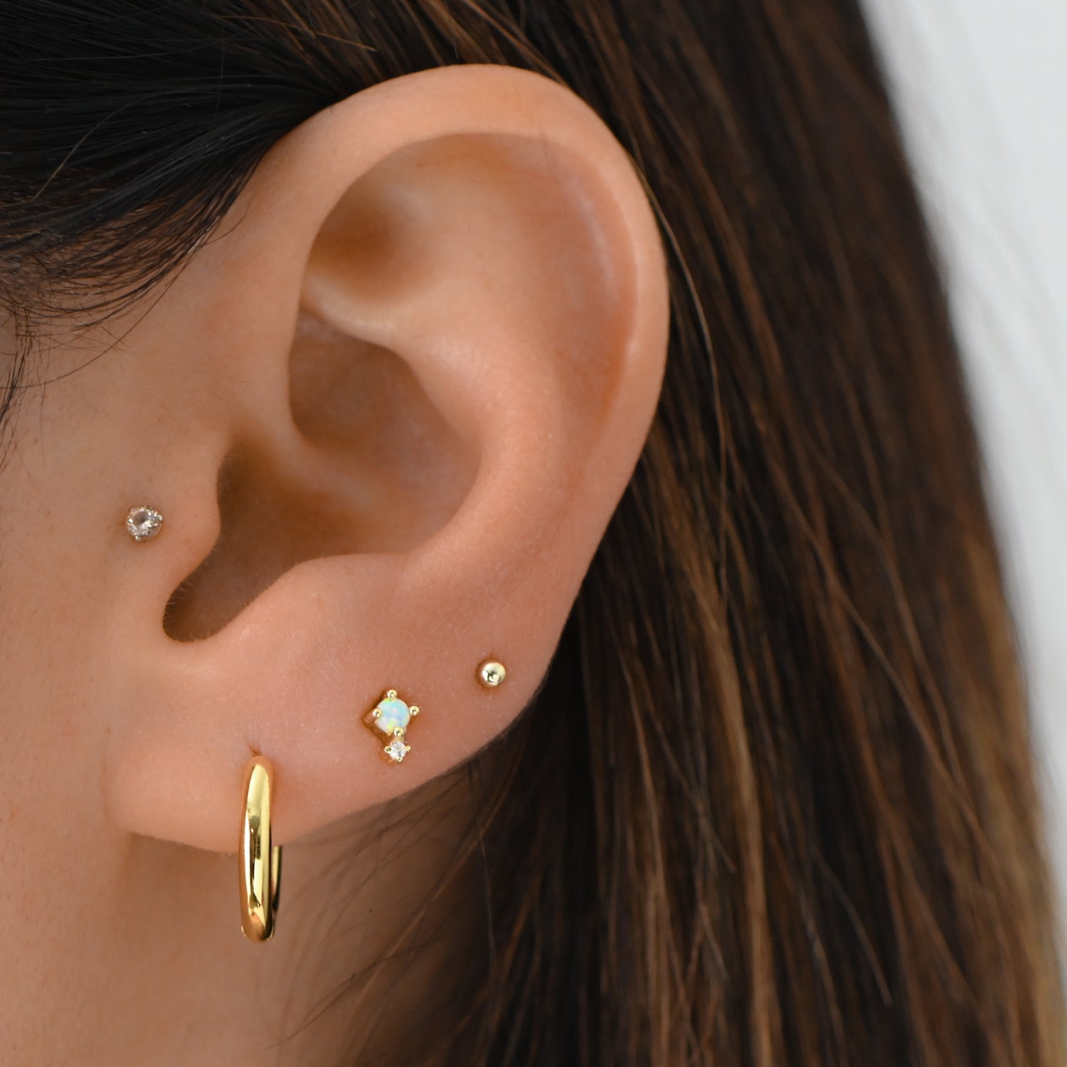 Model wearing gorgeous gold dainty hoop earrings paired with opal cz stud earrings and simple ball studs. 
